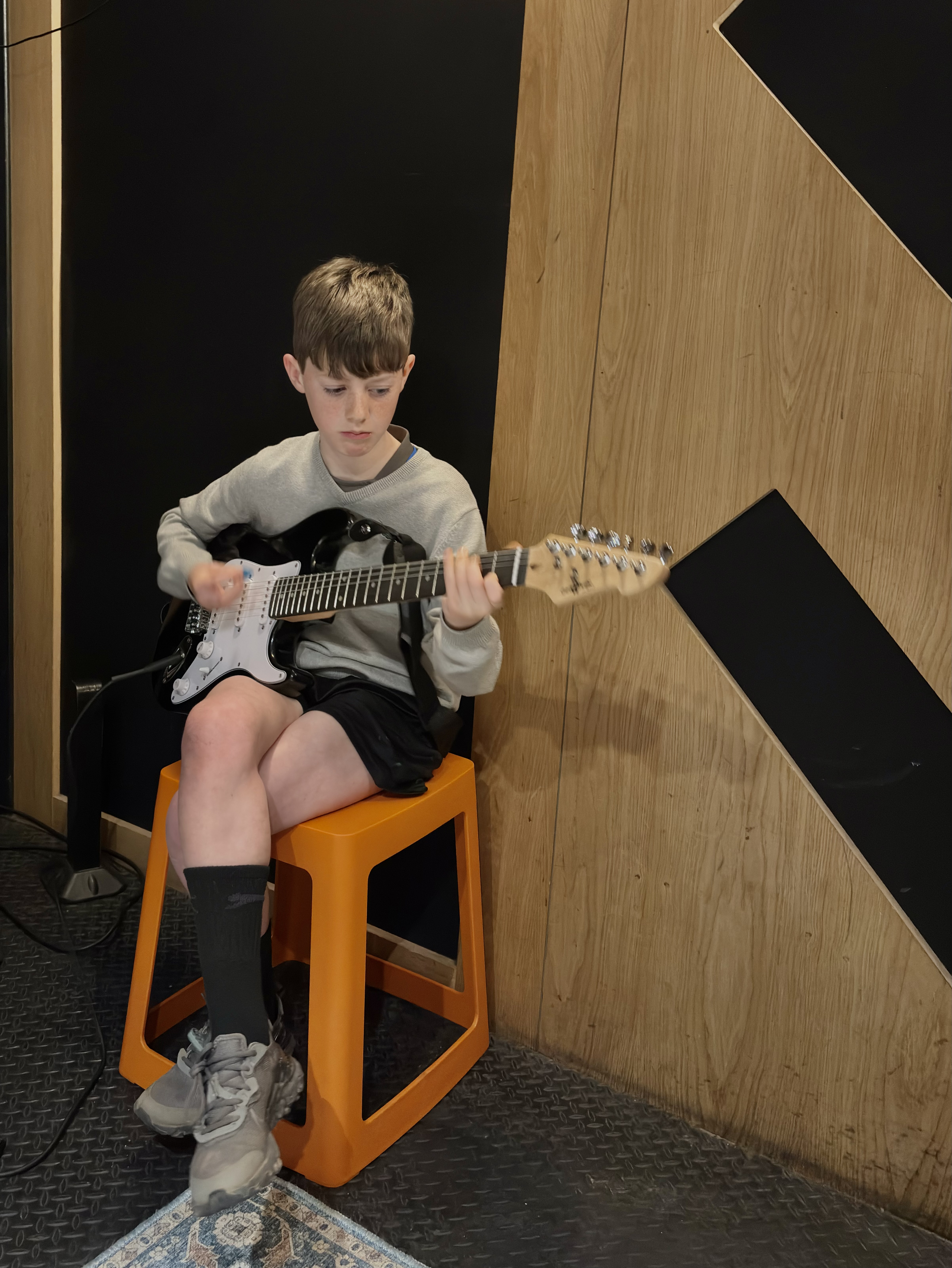 Child seated with an electric guitar during a Band Night session.